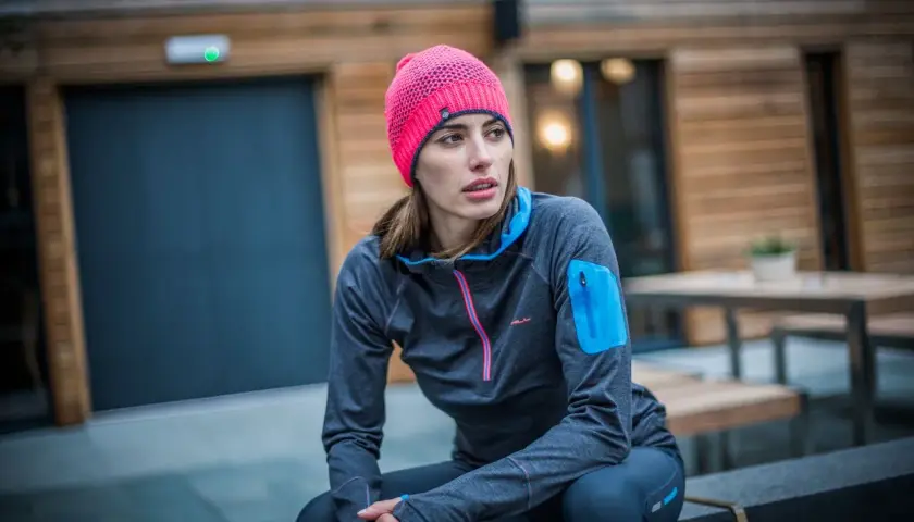 Kobieta w różowej czapce i sportowej bluzie siedzi na zewnątrz.